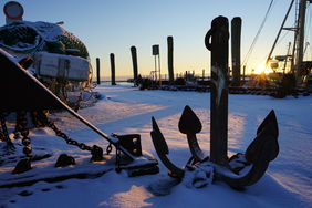 Pellworm im Winter, Verschneiter Pellwormer Hafen mit einem Anker im Vordergrund
